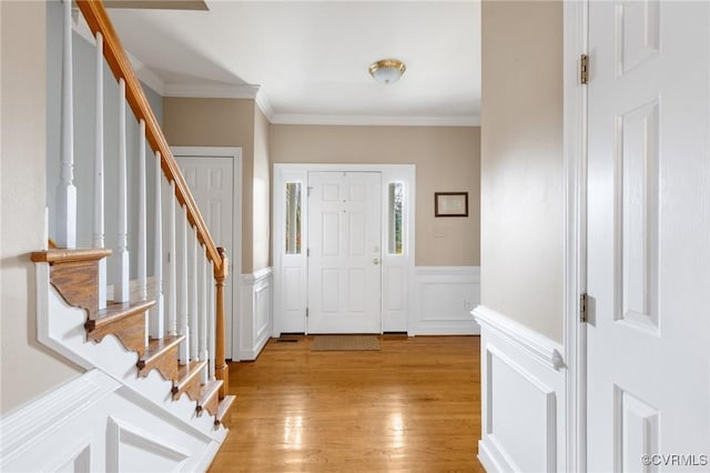 foyer entrance with a wainscoted wall, stairway, light wood-type flooring, ornamental molding, and a decorative wall