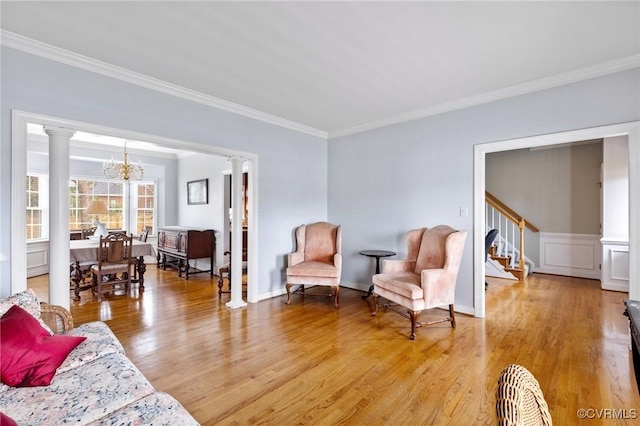 sitting room featuring light wood-style flooring, stairway, an inviting chandelier, crown molding, and ornate columns