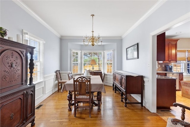 dining space with a wealth of natural light, an inviting chandelier, wainscoting, and light wood finished floors