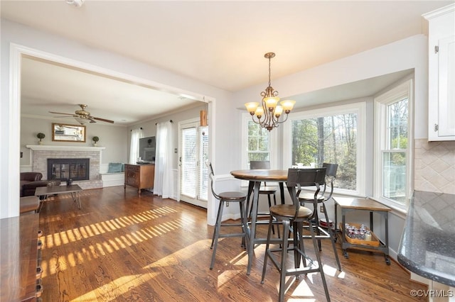 dining area with a glass covered fireplace, crown molding, ceiling fan with notable chandelier, and wood finished floors