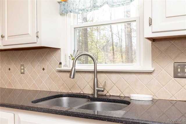 kitchen with a sink, tasteful backsplash, white cabinets, and dark stone countertops