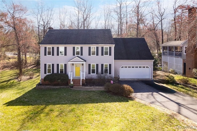 colonial home featuring driveway, a front yard, an attached garage, and a chimney