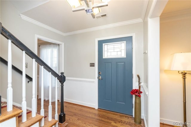 foyer entrance with visible vents, plenty of natural light, wood finished floors, and ornamental molding