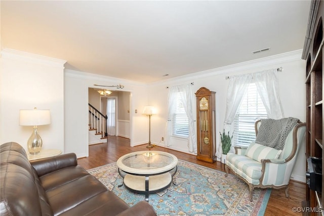 living room with stairs, wood finished floors, visible vents, and ornamental molding