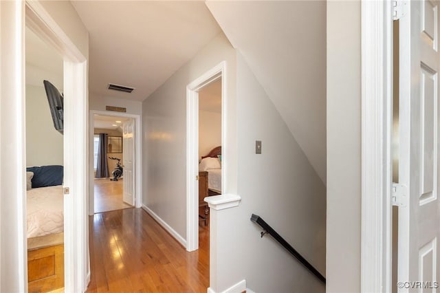 corridor with light wood-style floors, an upstairs landing, visible vents, and baseboards