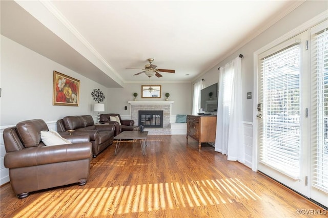 living room with a glass covered fireplace, ceiling fan, wood finished floors, and ornamental molding