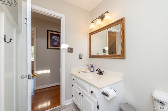 half bathroom with baseboards, toilet, wood finished floors, and vanity