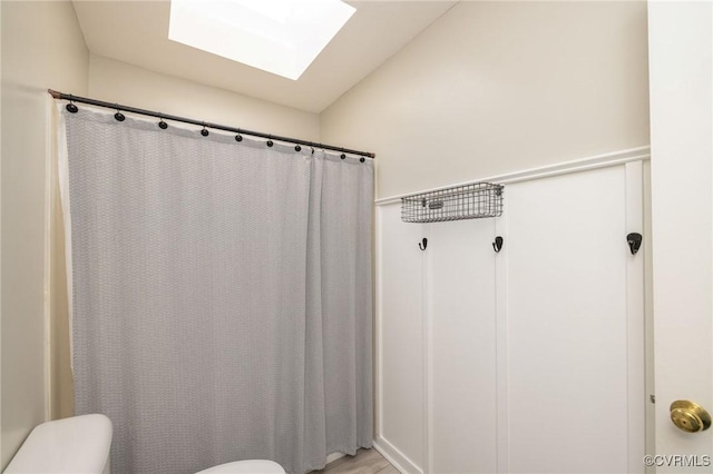 bathroom with a shower with curtain, a skylight, and toilet