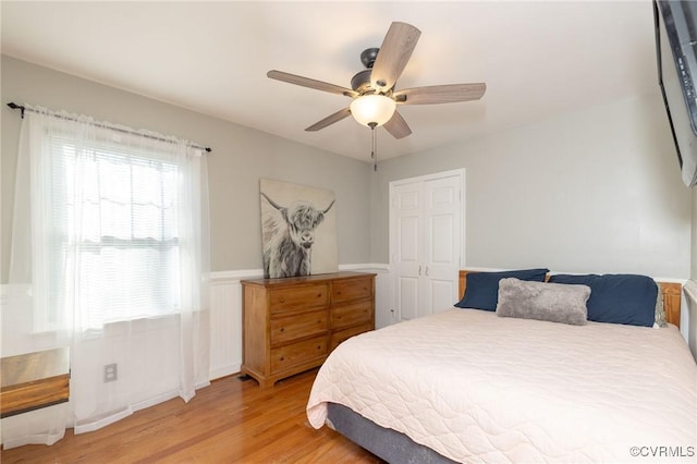 bedroom featuring wainscoting, light wood-type flooring, and ceiling fan