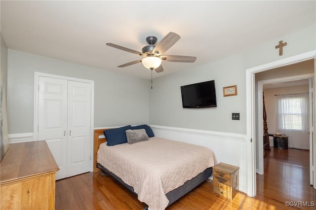 bedroom featuring a wainscoted wall, a closet, light wood-style flooring, and a ceiling fan