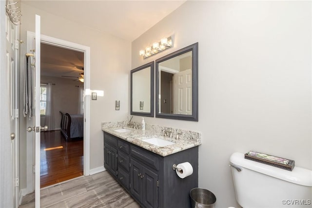 ensuite bathroom with double vanity, toilet, wood finished floors, and a sink