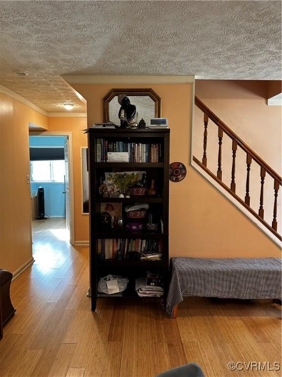 hall with ornamental molding, wood finished floors, baseboards, and a textured ceiling