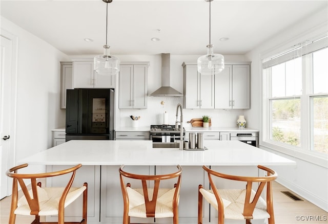 kitchen featuring visible vents, black fridge, wall chimney range hood, backsplash, and light countertops