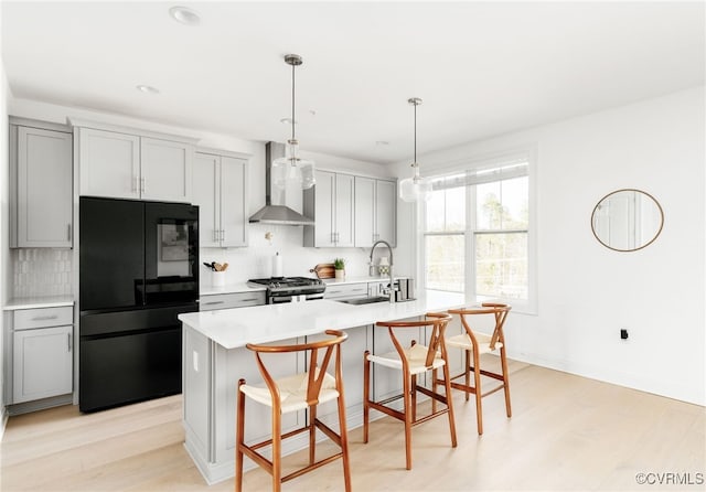 kitchen with stainless steel range with gas stovetop, freestanding refrigerator, light countertops, wall chimney exhaust hood, and tasteful backsplash