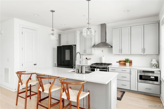 kitchen with light wood finished floors, a sink, light countertops, appliances with stainless steel finishes, and wall chimney exhaust hood