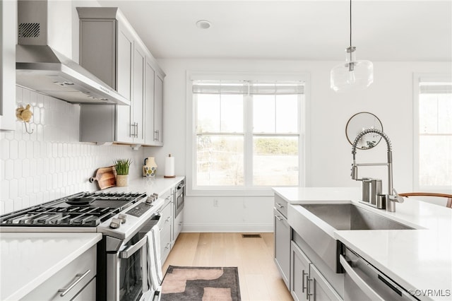 kitchen with appliances with stainless steel finishes, wall chimney exhaust hood, gray cabinets, and light countertops