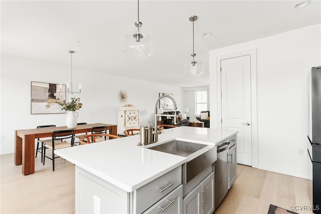 kitchen featuring light wood finished floors, a sink, hanging light fixtures, light countertops, and stainless steel appliances