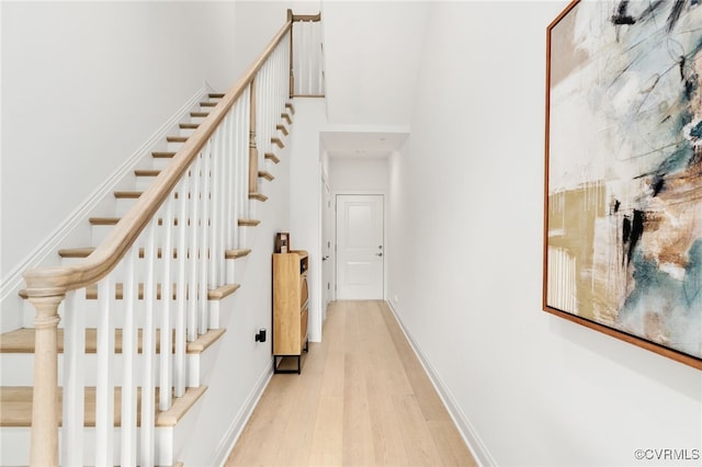 hall featuring stairs, a high ceiling, baseboards, and light wood finished floors