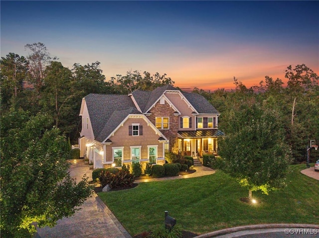 view of front of house with covered porch, a lawn, a garage, stone siding, and driveway