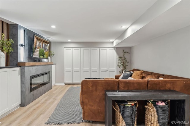 living room featuring recessed lighting, light wood-type flooring, and a glass covered fireplace