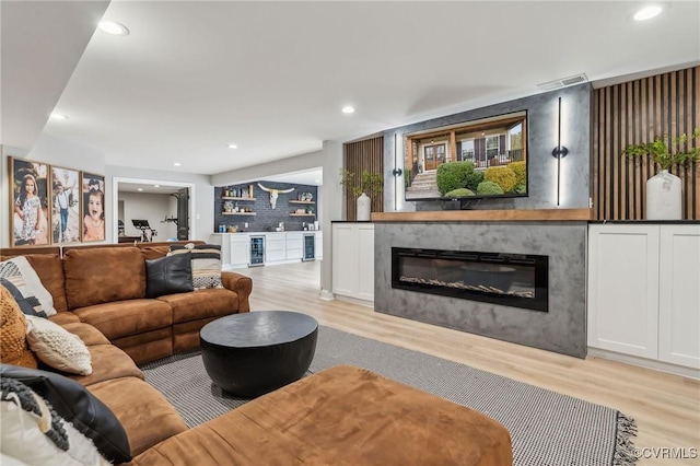 living area featuring visible vents, a glass covered fireplace, recessed lighting, light wood finished floors, and indoor bar