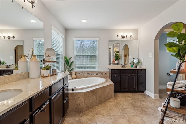 bathroom with tile patterned flooring, two vanities, a garden tub, and a sink