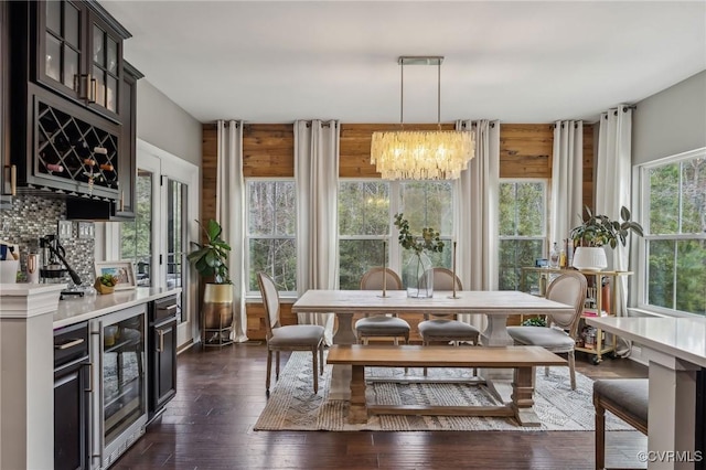 dining area featuring a chandelier, beverage cooler, a bar, and dark wood-style floors