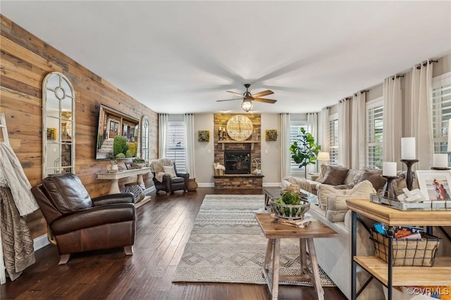 living area featuring baseboards, ceiling fan, wood walls, a stone fireplace, and wood-type flooring