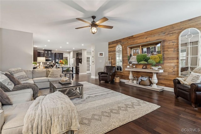 living room featuring baseboards, dark wood finished floors, wood walls, recessed lighting, and a ceiling fan