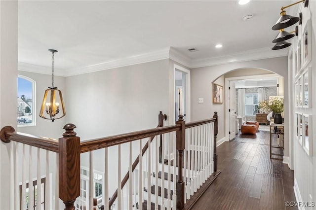 hallway featuring an upstairs landing, dark wood-type flooring, ornamental molding, plenty of natural light, and arched walkways