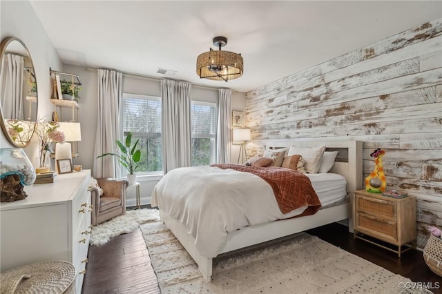 bedroom featuring an accent wall, wood finished floors, visible vents, and baseboards