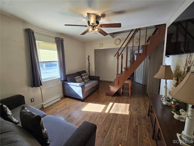 living room featuring a ceiling fan, stairway, wood finished floors, and baseboard heating