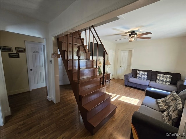 living room featuring stairs, baseboards, dark wood-style flooring, and ceiling fan