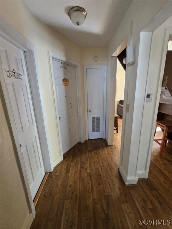 hallway featuring visible vents, dark wood-type flooring, and baseboards