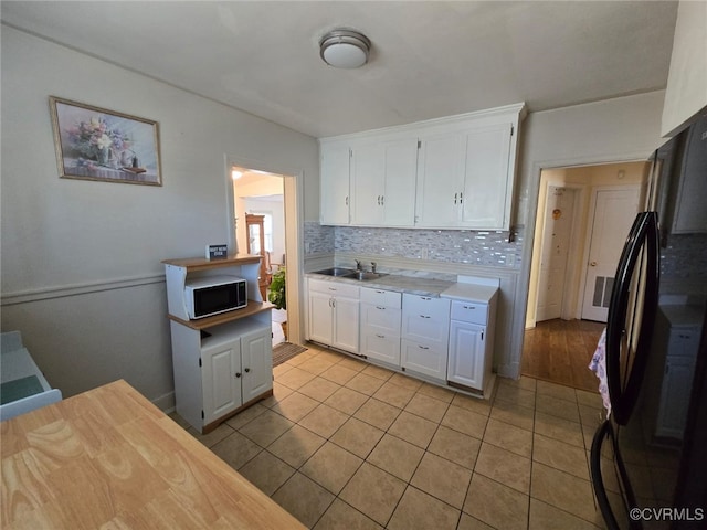 kitchen with backsplash, white cabinetry, freestanding refrigerator, and light countertops