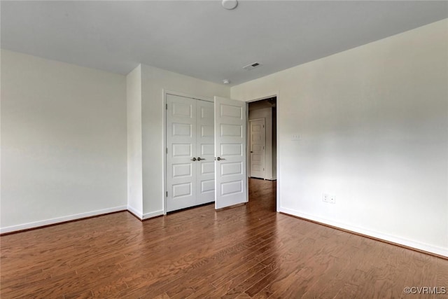 unfurnished bedroom with dark wood-style floors, visible vents, a closet, and baseboards