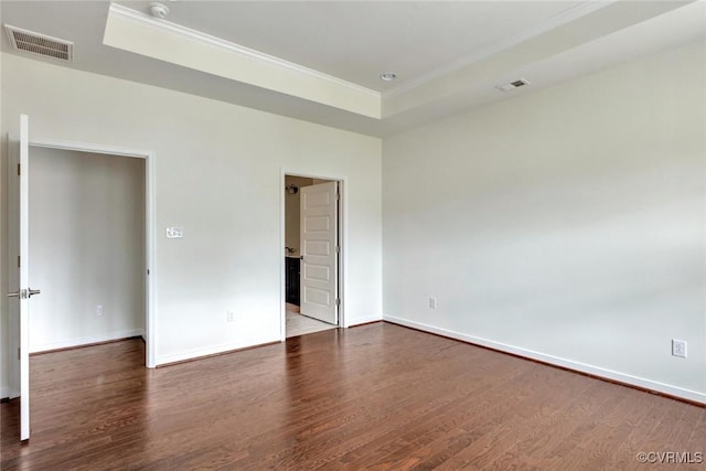 unfurnished bedroom featuring a tray ceiling, visible vents, baseboards, and dark wood-style flooring