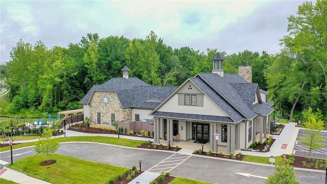 view of front of home featuring a front yard, fence, a porch, a shingled roof, and stone siding