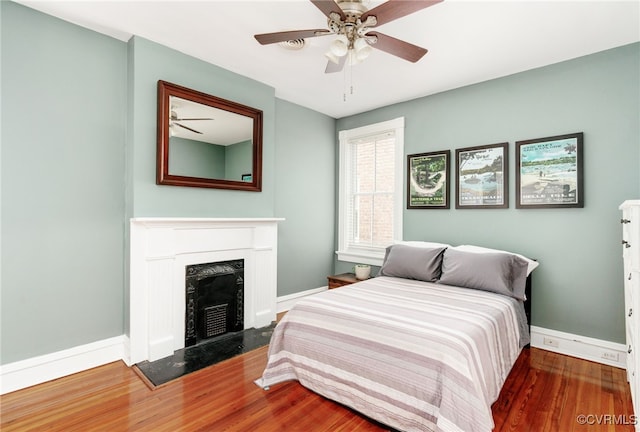 bedroom with ceiling fan, a premium fireplace, baseboards, and wood finished floors