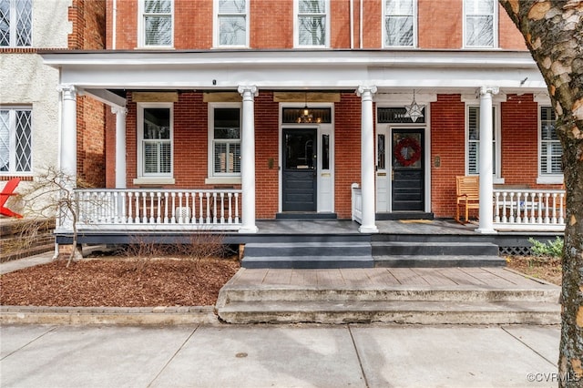 view of exterior entry featuring brick siding and covered porch