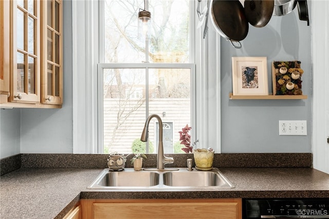 kitchen with dishwasher, dark countertops, glass insert cabinets, and a sink