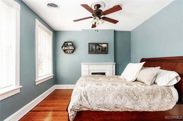 bedroom with visible vents, a ceiling fan, wood finished floors, a fireplace, and baseboards