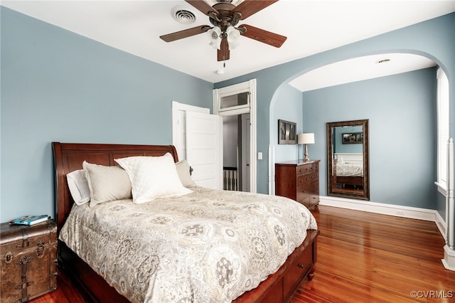 bedroom featuring a ceiling fan, baseboards, wood finished floors, visible vents, and arched walkways