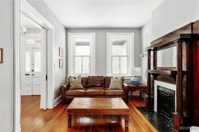 living room featuring baseboards, a fireplace with flush hearth, and hardwood / wood-style flooring