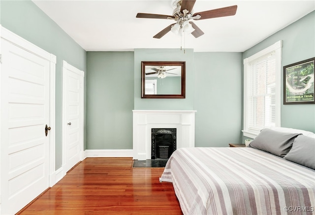 bedroom with a high end fireplace, ceiling fan, baseboards, and wood finished floors