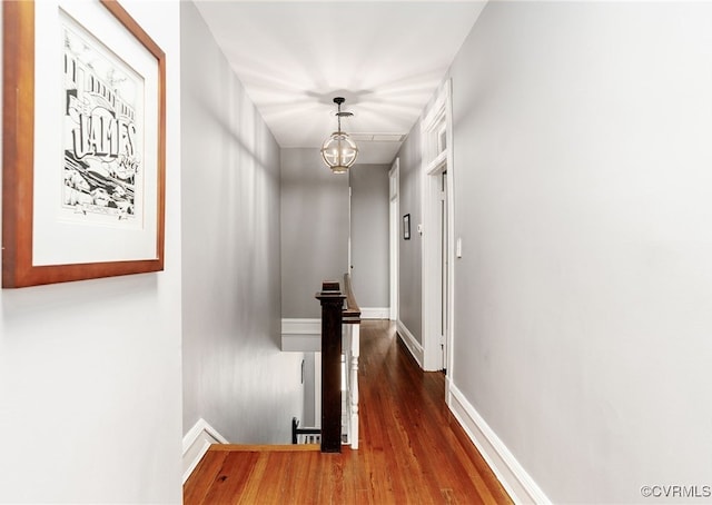 hallway featuring a chandelier, baseboards, and wood finished floors