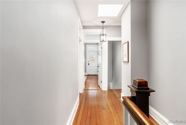 hall with a skylight, light wood-style floors, and baseboards