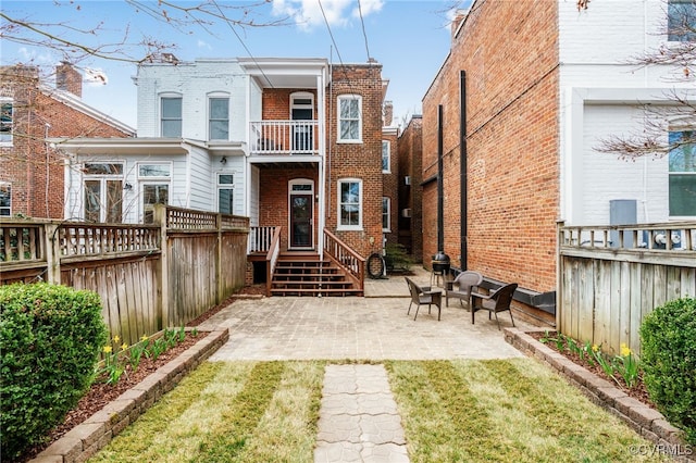 back of house featuring a balcony, a patio area, brick siding, and fence private yard