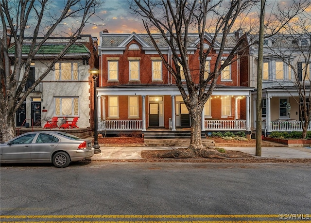 townhome / multi-family property featuring covered porch and brick siding