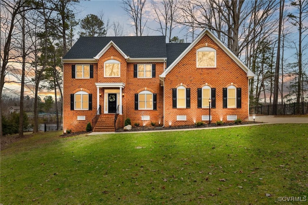 colonial home featuring crawl space, brick siding, a lawn, and a shingled roof